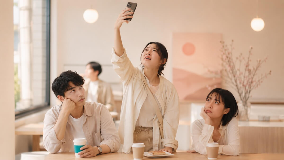 A stressed group of friends in a cafe in Tokyo, looking annoyed at one friend who is holding their phone high in the air trying to catch a weak free Wi-Fi signal.